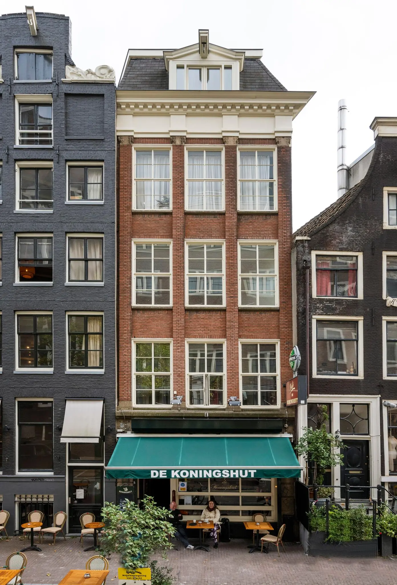 Voorgevel van het café De Koningshut met groen zonnescherm aan de Nieuwezijds Voorburgwal in Amsterdam.